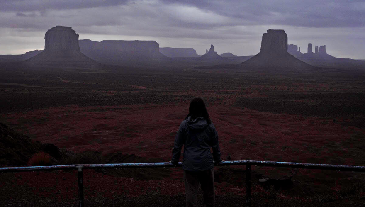 A girl looks out across the vast Monument Valley as a storm rages overhead.