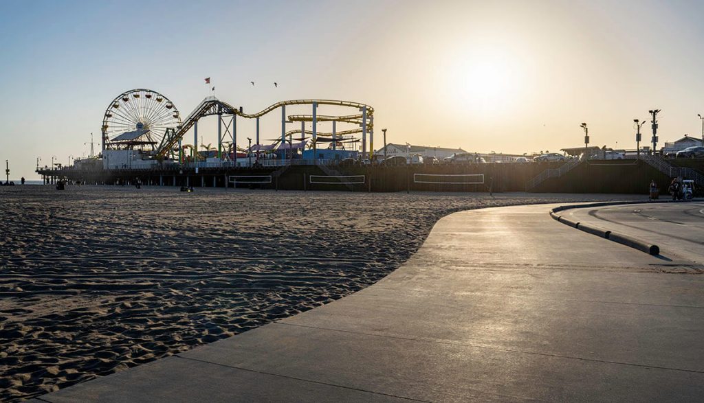 The sun set below the Santa Monica Pier with the carnival rides and soft sand in the foreground.