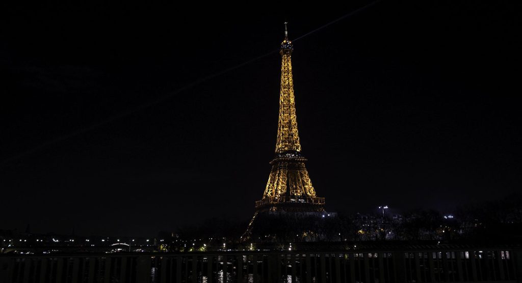 The tower sparkles in the night sky above the river from one of the best Eiffel Tower views.