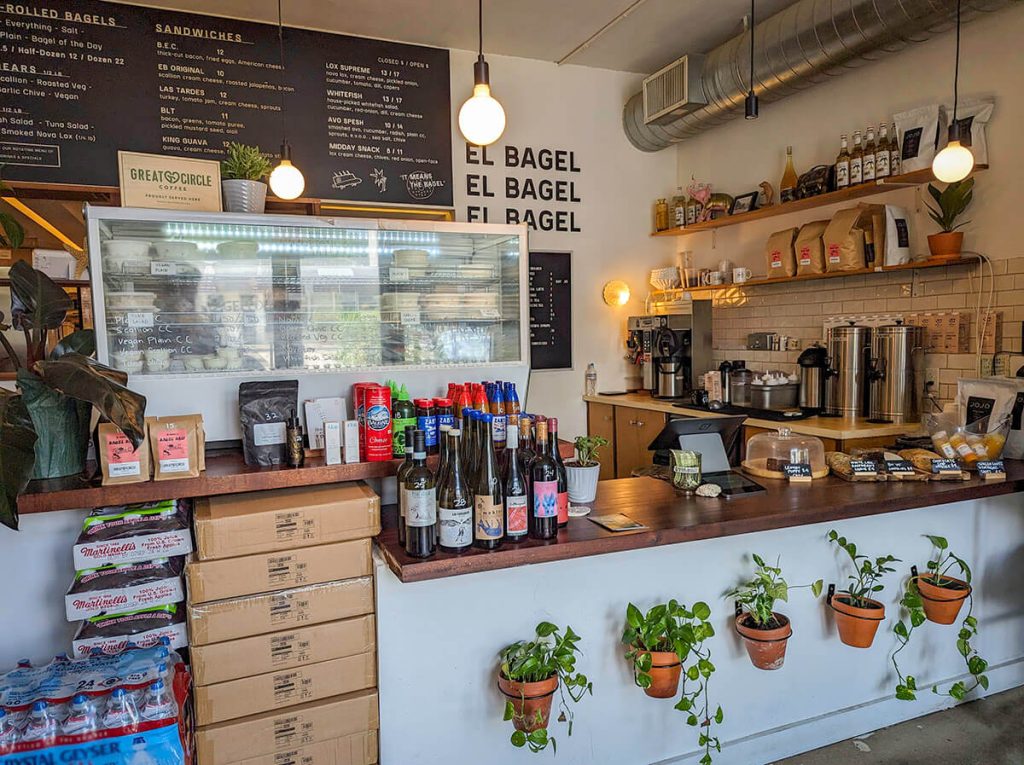 Inside the welcoming bagel shop of El Bagel with a large menu and potted plants.