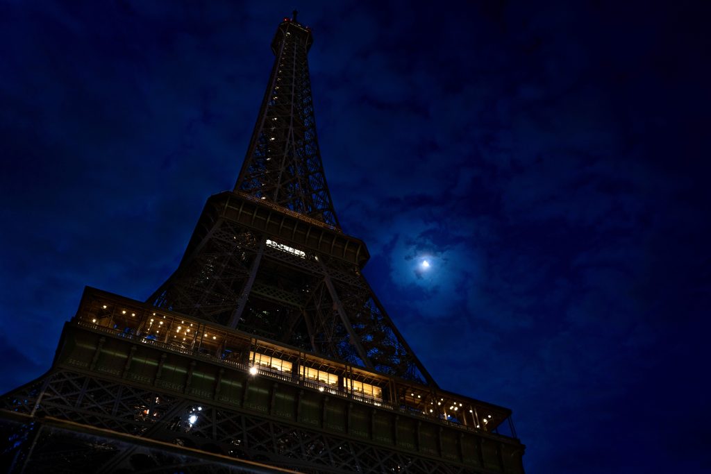 Looking up at the unlit tower at night with the bright moon watching above.