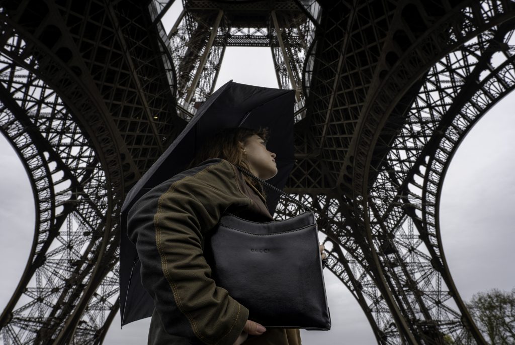 A woman stands underneath the Eiffel Tower as the iron frames shoot up to the sky.