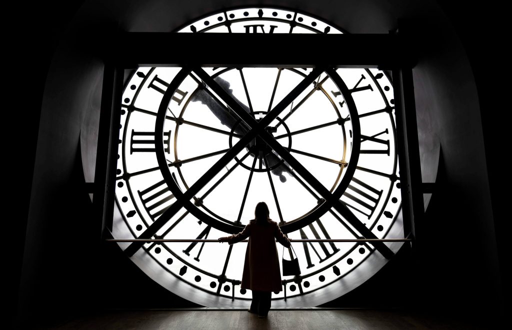 a woman stands in front of a giant clock at a Paris museum